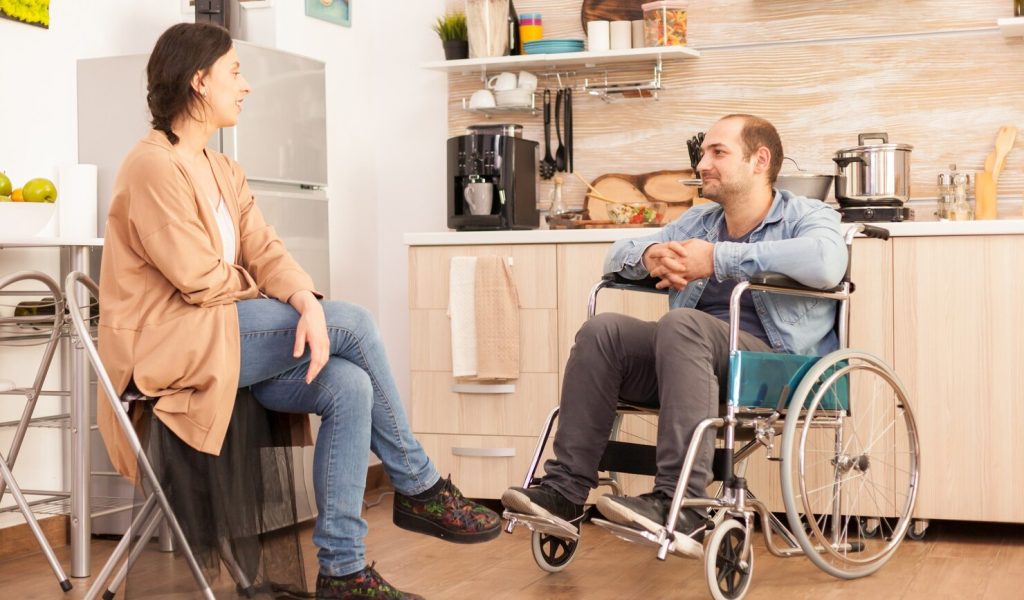 handicapped-man-wheelchair-looking-caring-wife-kitchen-disabled-paralyzed-handicapped-man-with-walking-disability-integrating-after-accident_482257-10625