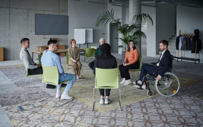 In a modern office, a diverse group of business individuals is seen gathered in a circle, engaged in lively discussions and sharing ideas about various business concepts