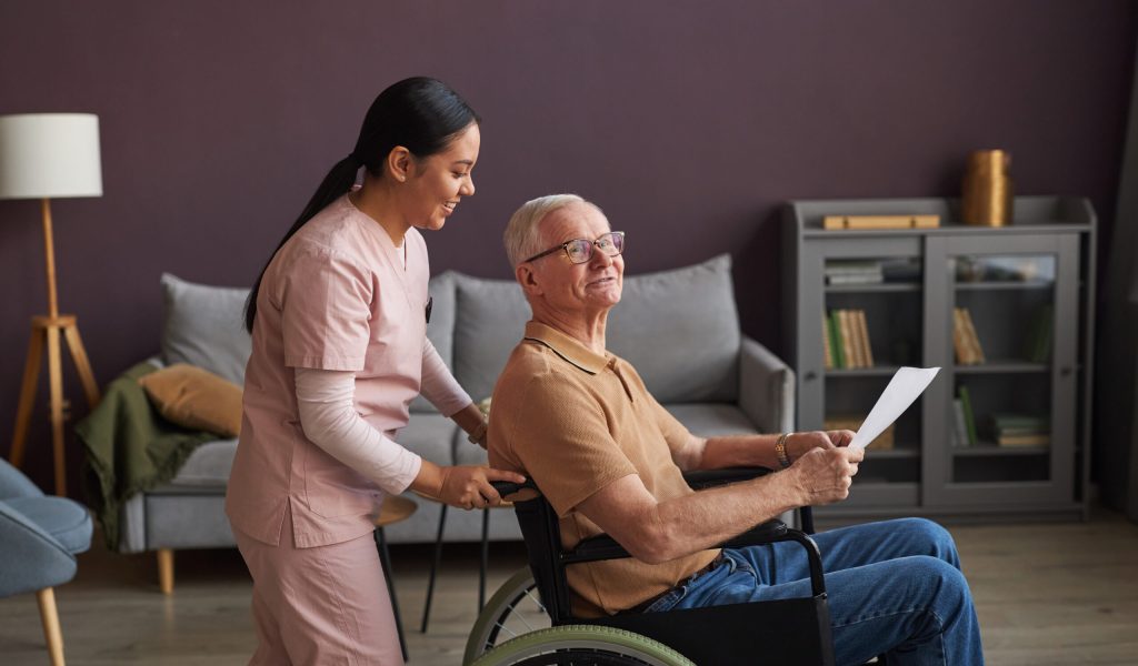 Young social worker pushing the wheelchair and helping senior man with documents and bills